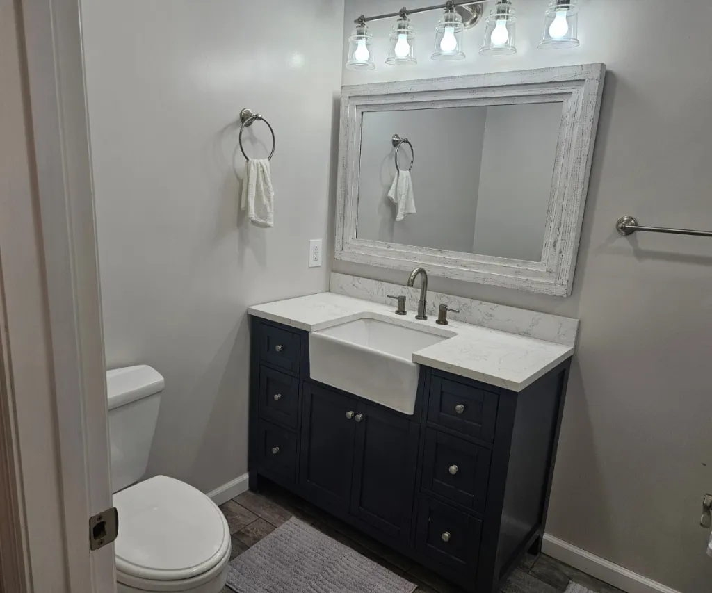 Navy vanity with a farmhouse sink, a framed mirror and a four-light bar