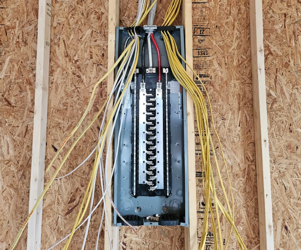 Breaker panel set in a wall with yellow cable pulled in for rough-in