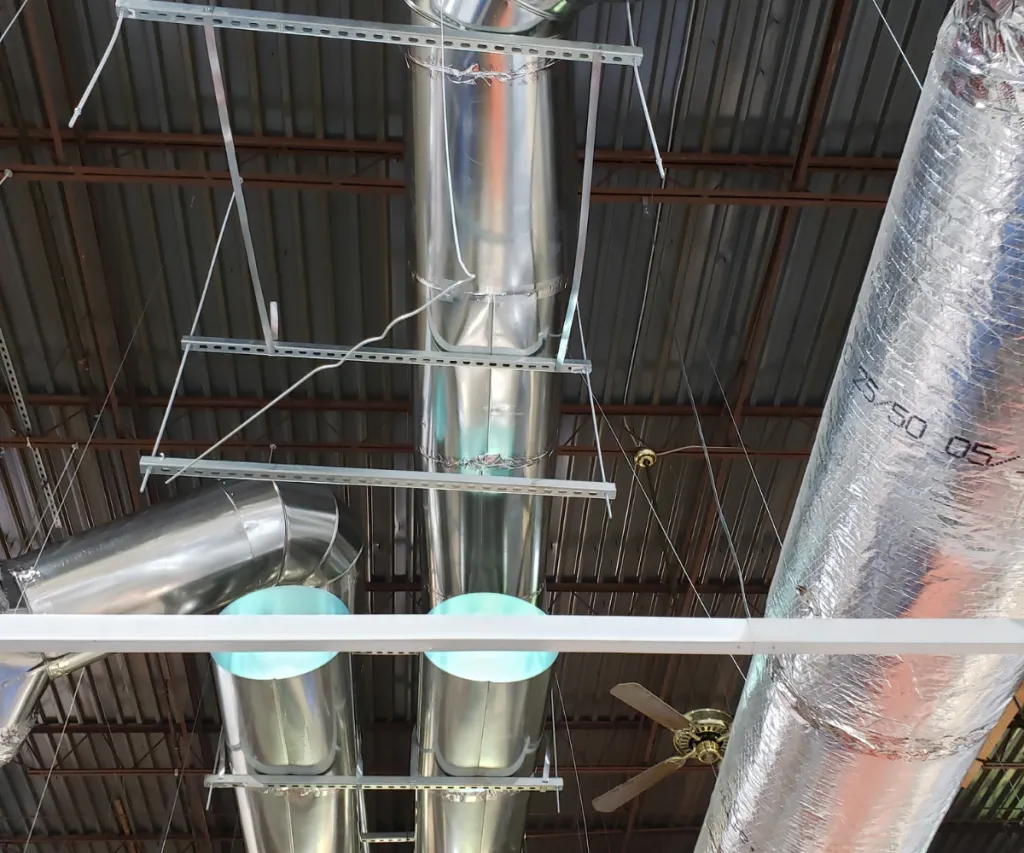 Light fixtures and strut hung from an open steel ceiling beside insulated duct