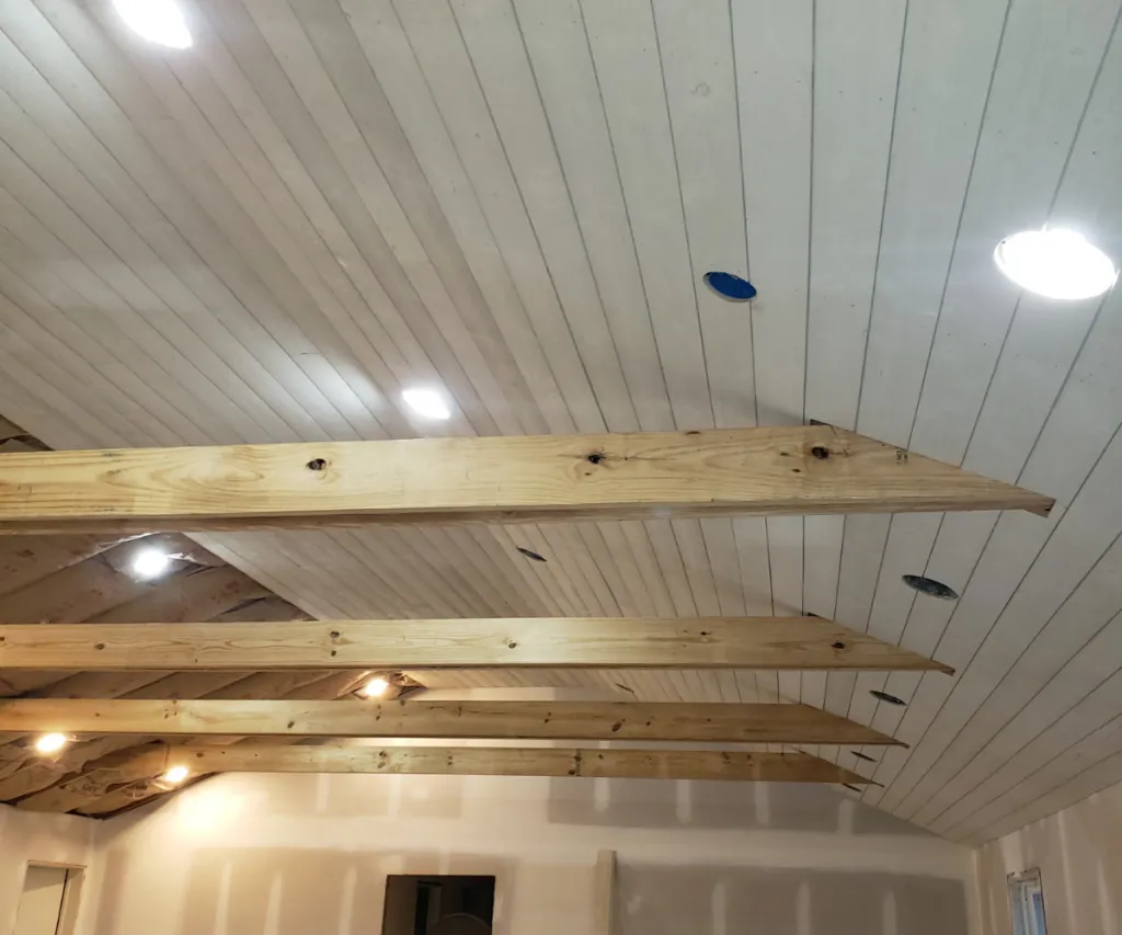 White shiplap ceiling with wood beams and recessed lights switched on
